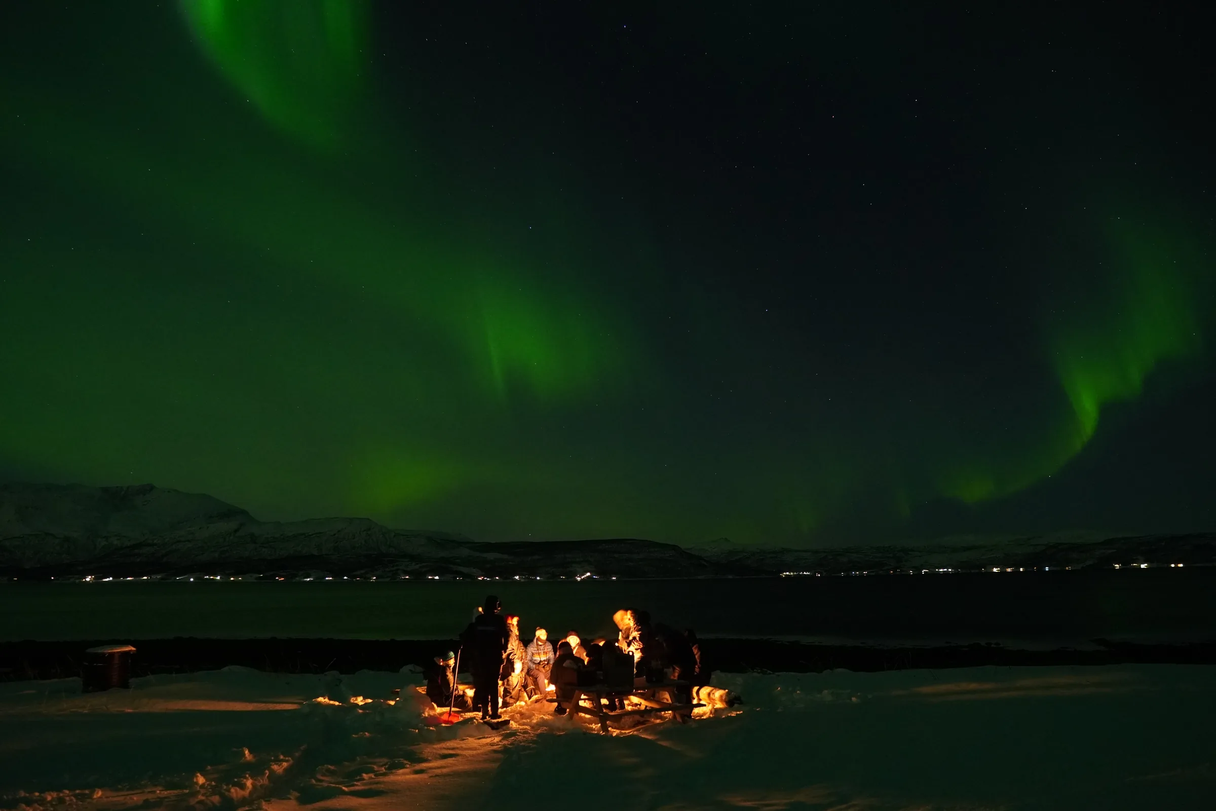 Grupo alrededor de una fogata bajo la aurora boreal en la Laponia finlandesa